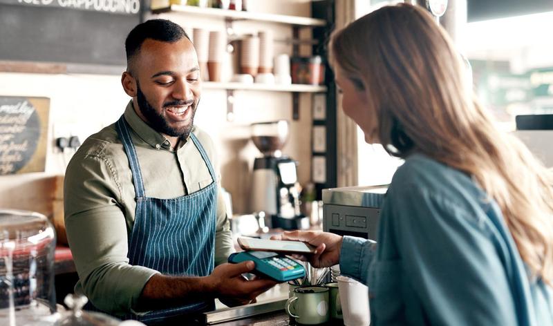 Young man accepting a digital payment from a customer in a cafe